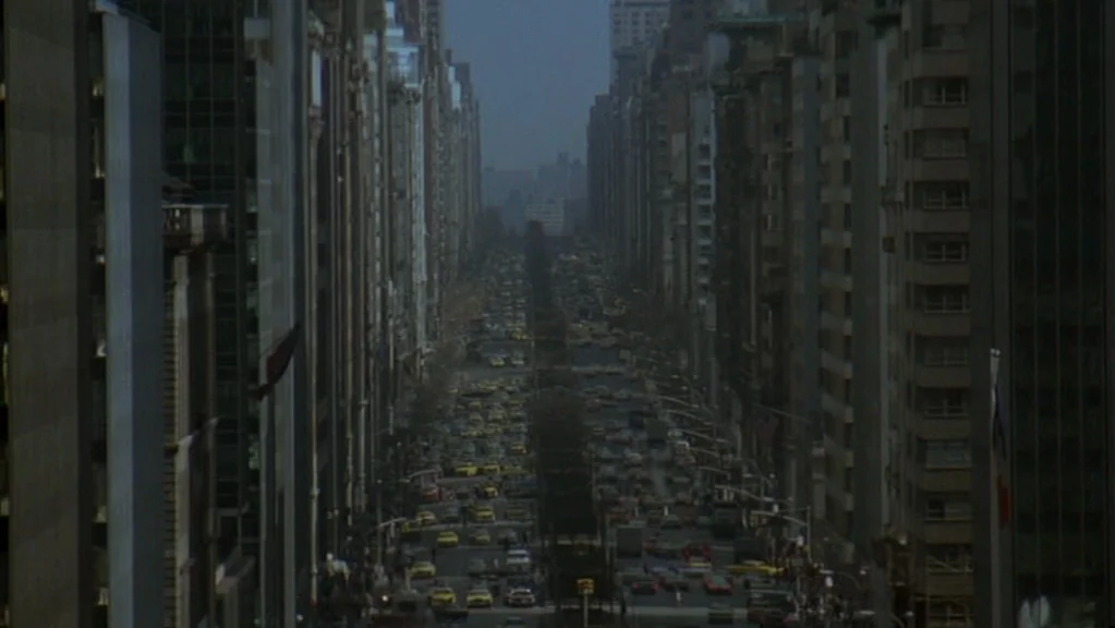 Magic (1978) movie still: establishing — A long, straight New York City avenue is flanked by tall, dark corporate buildings. Numerous yellow taxis…