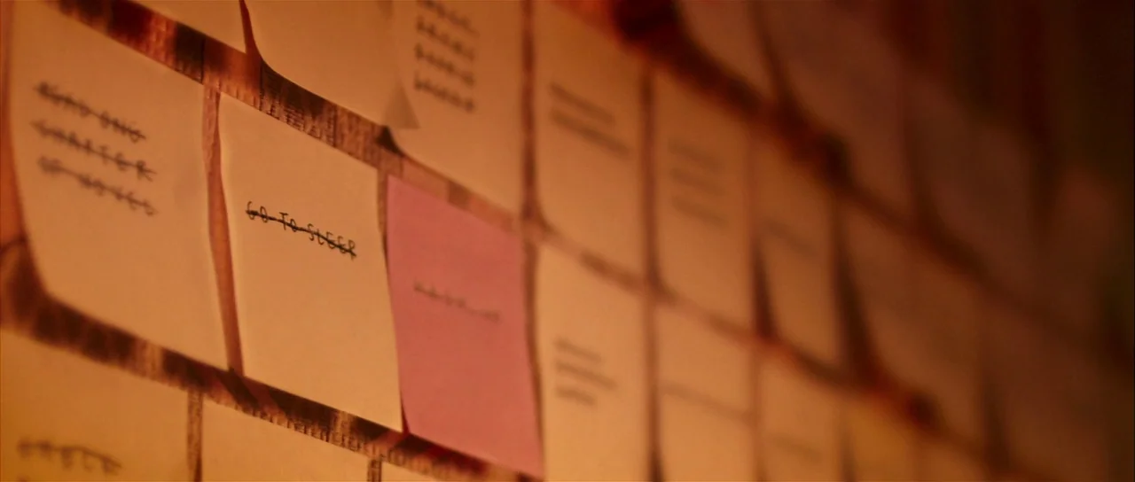 Bunny and the Bull (2009) movie still: closeup — A wall covered in numerous square sticky notes arranged in a grid pattern. Each note contains…