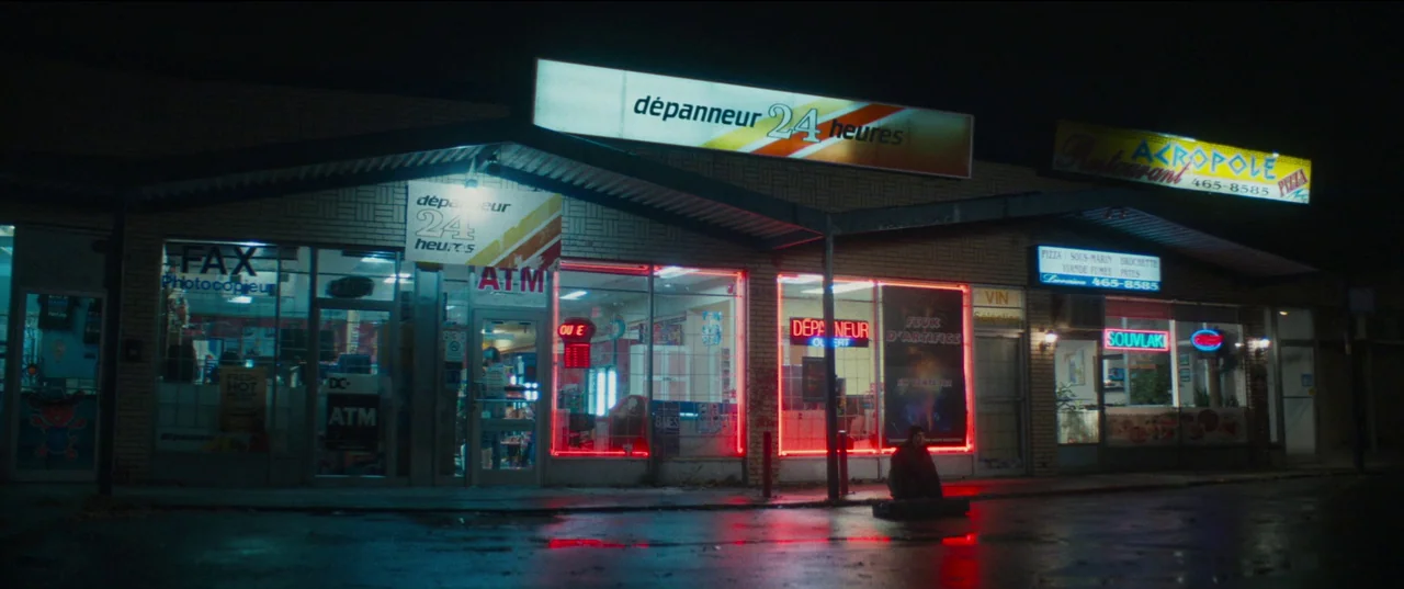 Humanist Vampire Seeking Consenting Suicidal Person (2023) movie still: wide — A roadside strip mall featuring a 24-hour convenience store under…