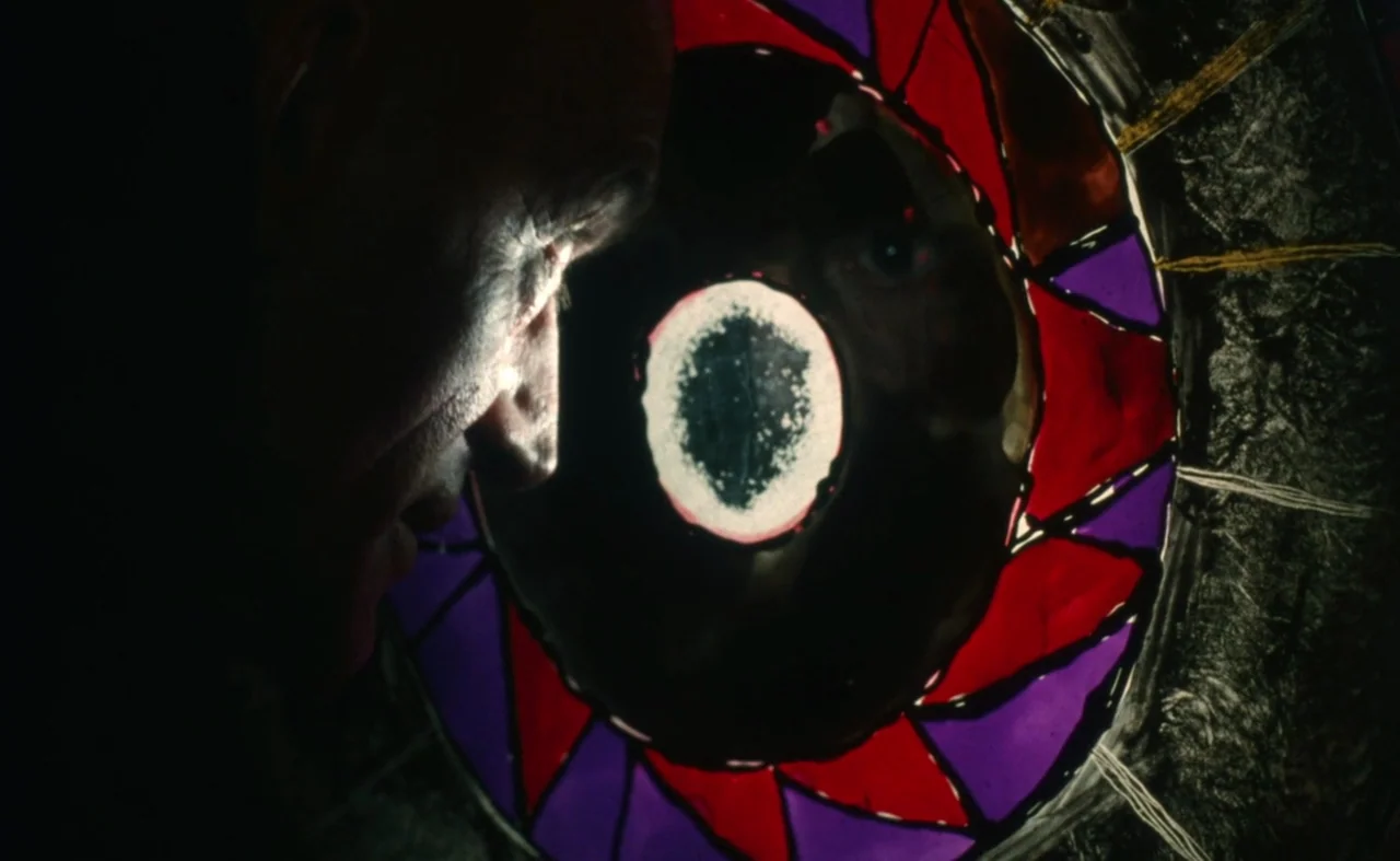 The Pit and The Pendulum (1991) movie still: closeup — A dark, dimly lit environment features a circular, multi-colored stained glass partition. A…