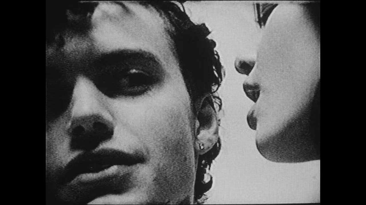 Divinity (2023) movie still: closeup — A close-up view of two individuals in a high-contrast black and white frame. One person looks toward the…