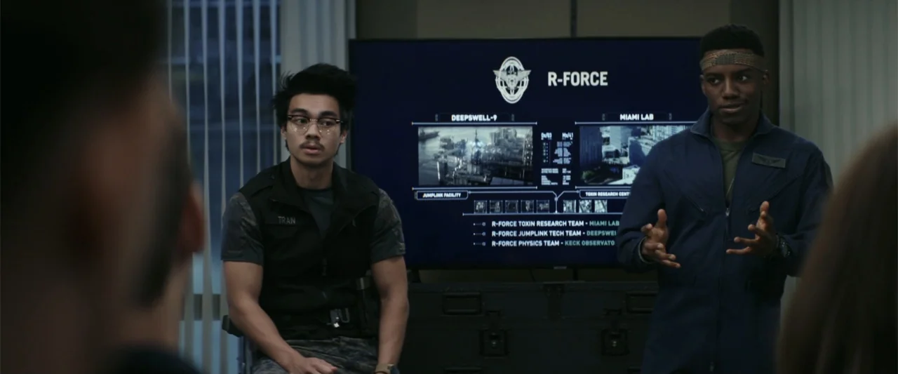 The Tomorrow War (2021) movie still: medium — A dimly lit room features a large digital screen displaying tactical data maps. Two men in uniform…