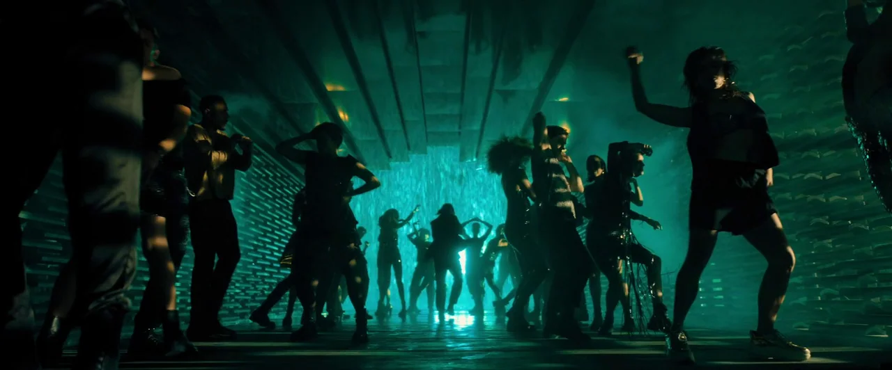 John Wick: Chapter 4 (2023) movie still: wide — A crowded dance floor in a dimly lit club with teal lighting. Silhouetted people move rhythmically…