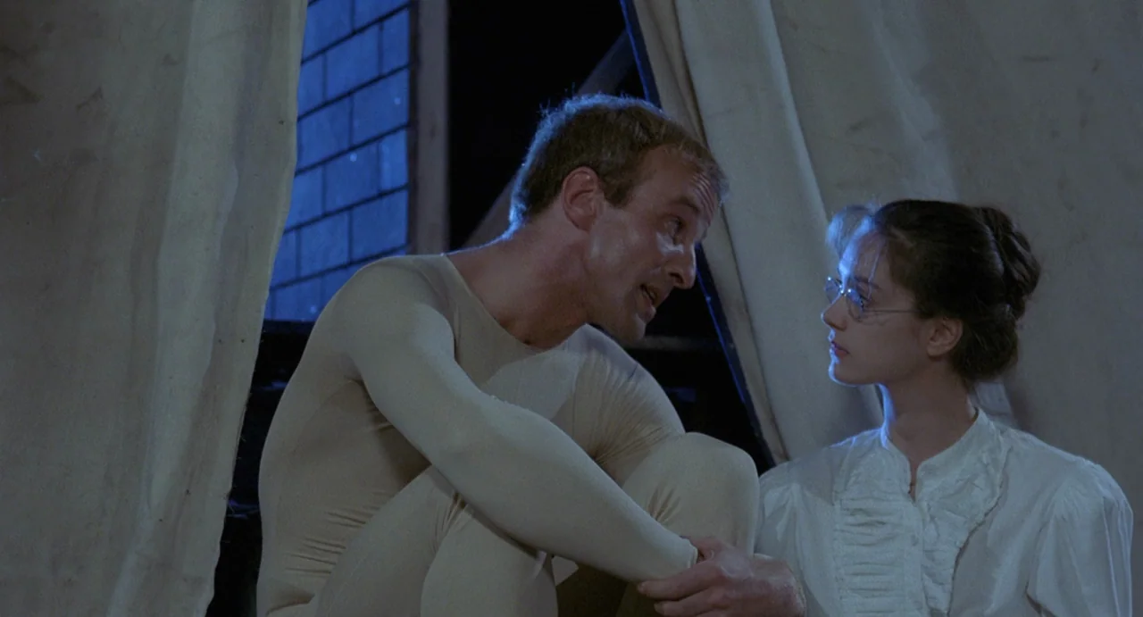 StageFright (1987) movie still: medium — A man and woman sit together in a dark space near an open window. They engage in conversation while…