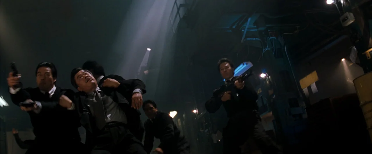 Lethal Weapon 4 (1998) movie still: medium — A dark, cluttered industrial space with heavy machinery and vertical light beams overhead. Several men…