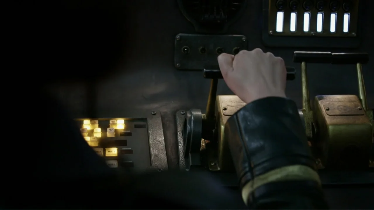 Mortal Engines (2018) movie still: closeup — A dimly lit industrial control console features brass lever handles and glowing interface buttons. A…