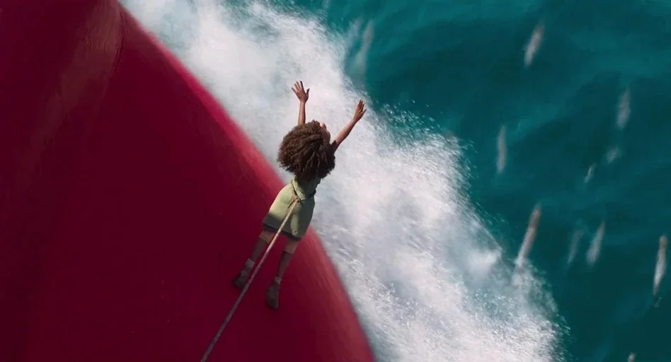 The Sea Beast (2022) movie still: wide — A bright red bow of a ship cuts through turquoise ocean water creating white foam. A small child stands on…