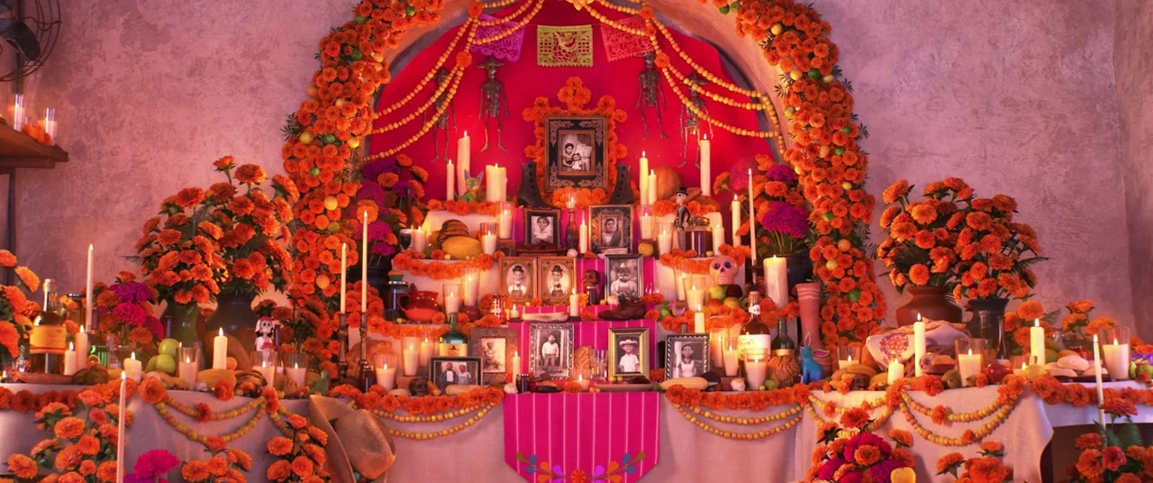 Coco (2017) movie still: wide — A traditional Day of the Dead ofrenda altar filled with marigolds and photographs. Multiple candles glow amidst…