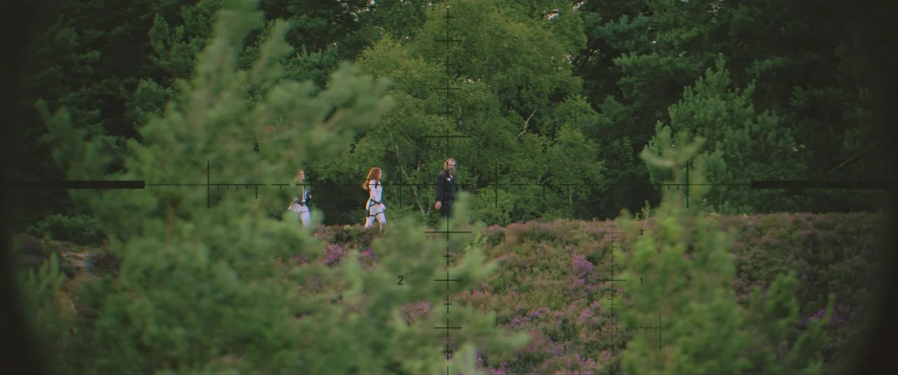 Black Widow (2021) movie still: wide — An open heath covered in purple heather with dense green trees in the background. Three people walk from left…