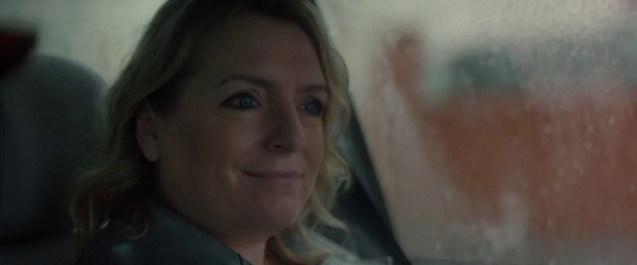 Ali & Ava (2021) movie still: closeup — A woman sits inside a car with the side window fogged with condensation. She looks forward with a smile…
