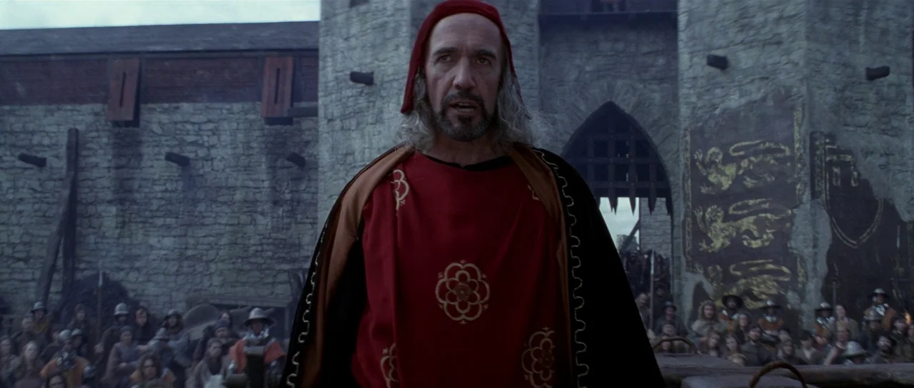 Braveheart (1995) movie still: medium — A stone fortification stands in the background with a portcullis visible. A man in period clothing stands…