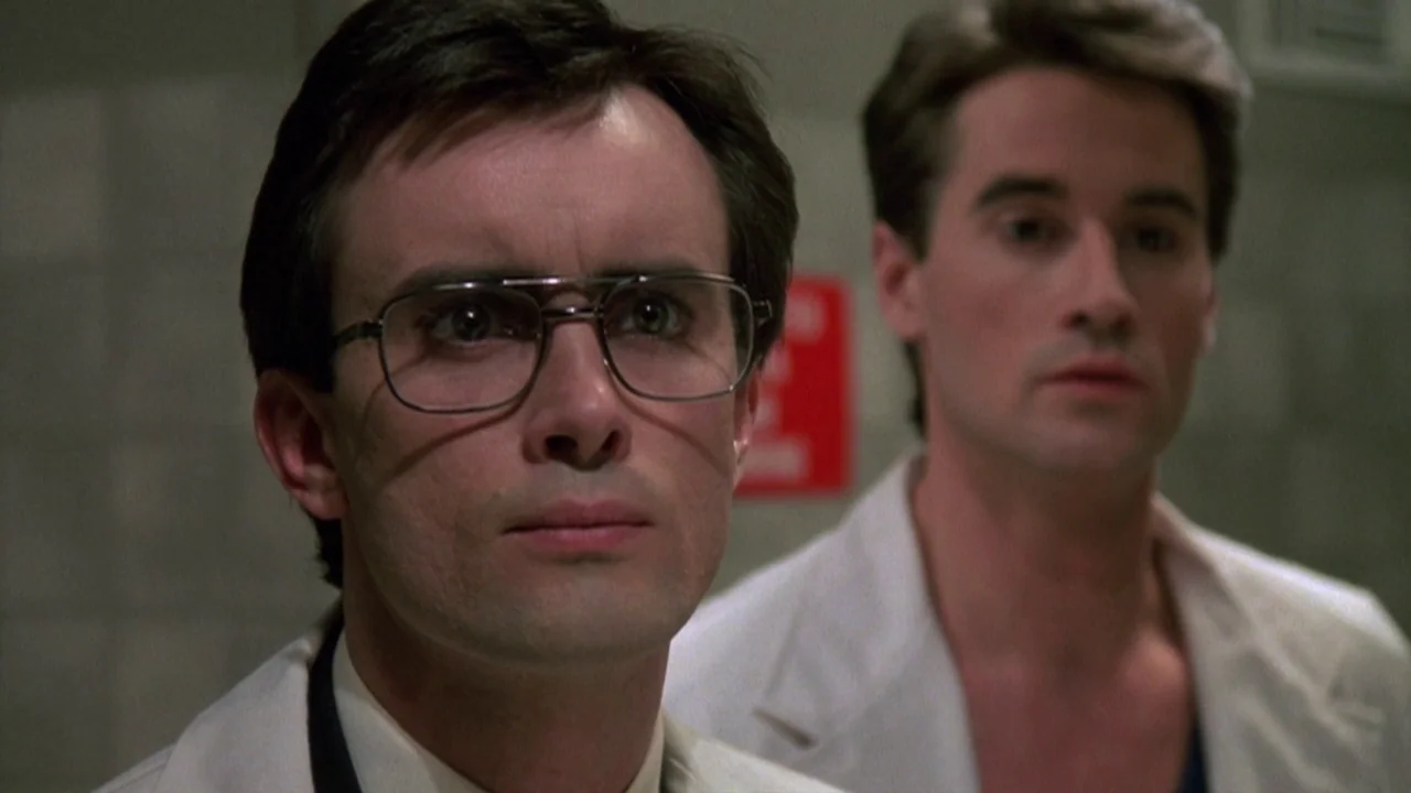 Re-Animator (1985) movie still: medium — A sterile room with grey-white tiled walls contains two men in lab coats. The men observe something…