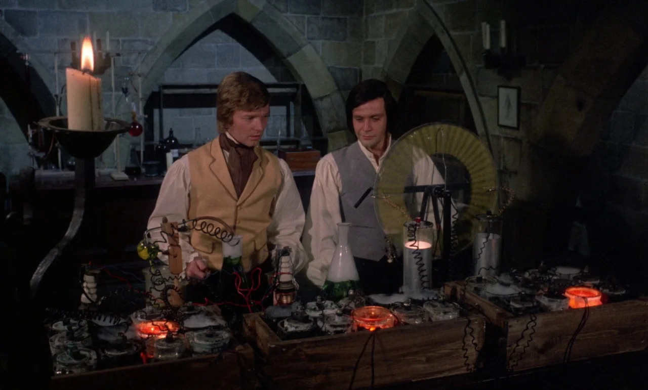 The Horror of Frankenstein (1970) movie still: medium — A stone-walled room with gothic arches features a cluttered wooden table filled with…