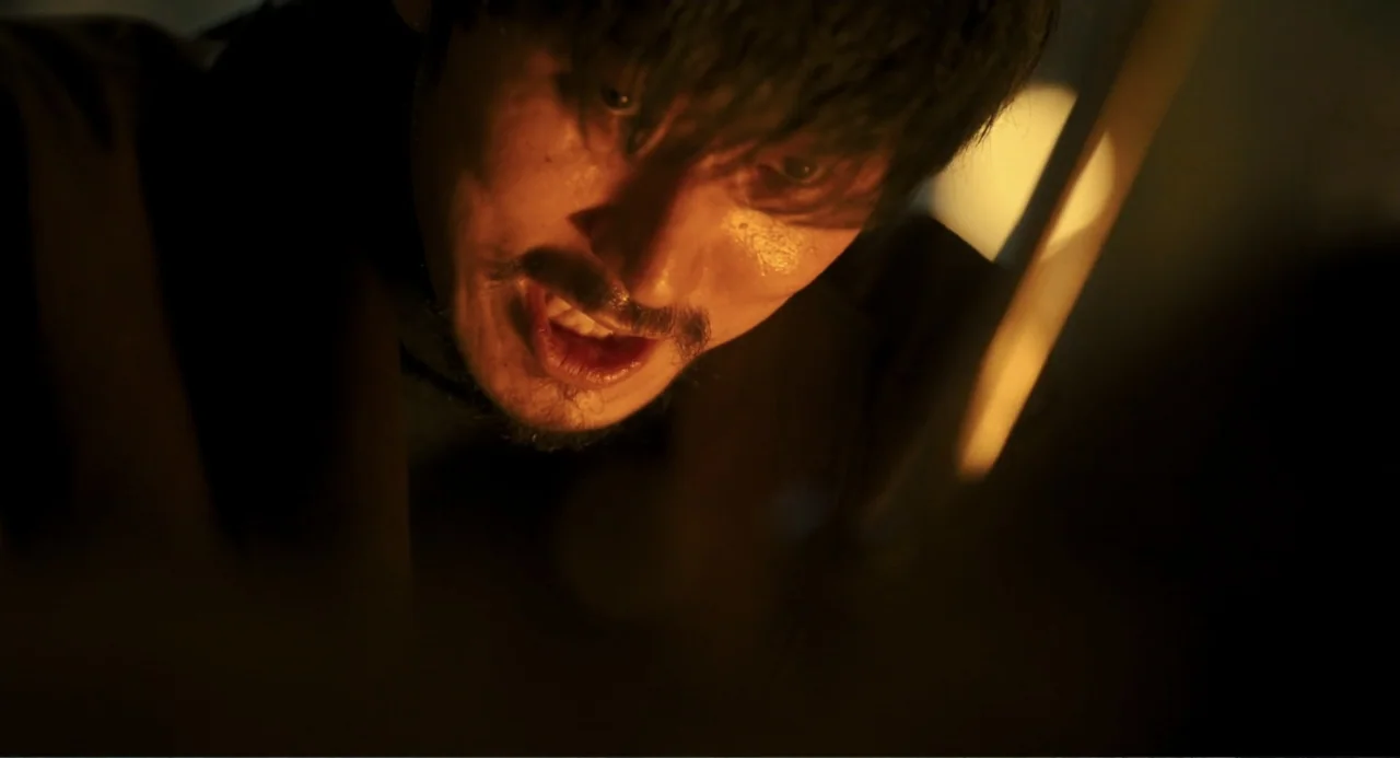 Knuckle Girl (2023) movie still: closeup — A dimly lit interior space with a man positioned in deep shadow. The subject tilts his head downward…
