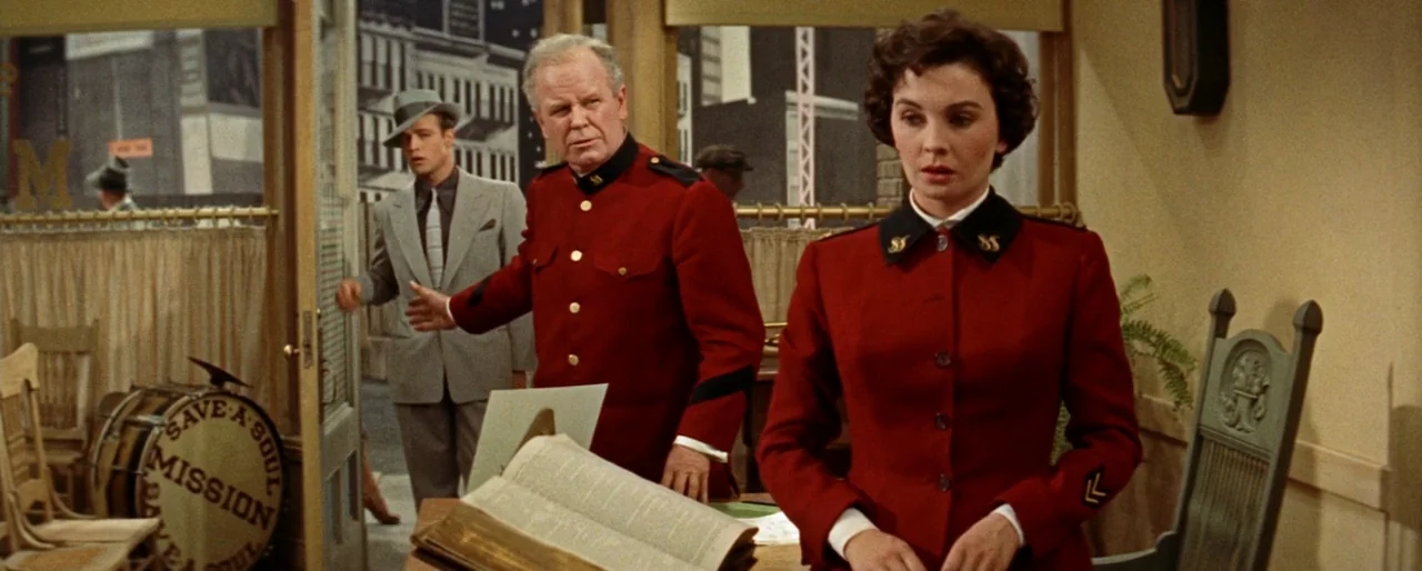 Guys and Dolls (1955) movie still: medium — An interior space with beige walls features a desk holding a large open book. A woman in a red uniform…