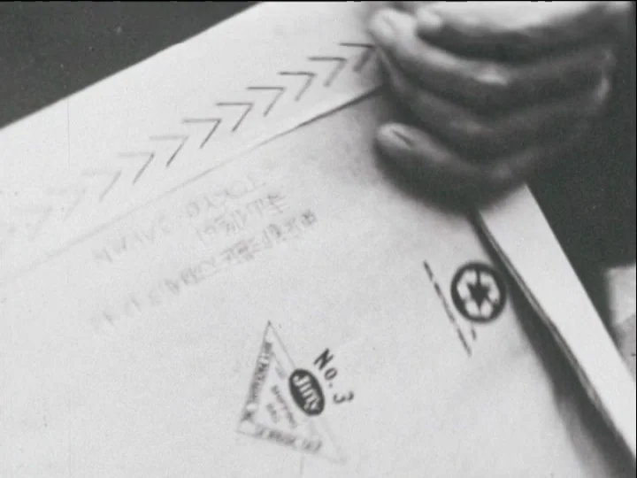 Catalogue of Memory (1977) movie still: closeup — A close-up of a manila envelope with shipping stamps and Japanese printed text. A person's hand…