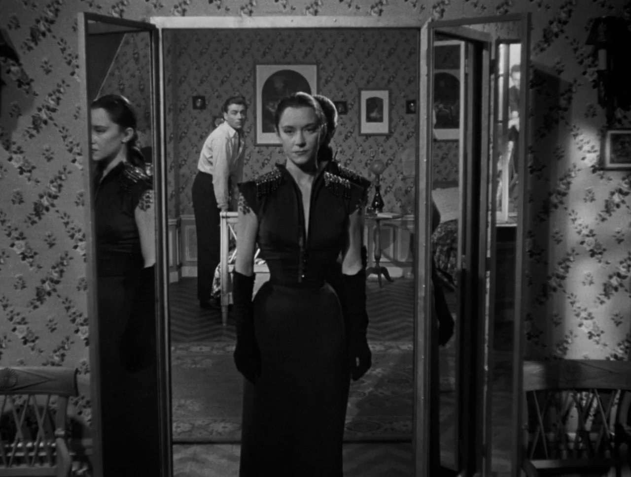 Orpheus (1950) movie still: fullbody — A room with patterned floral wallpaper features a central woman framed by large mirrors. A man stands near a…