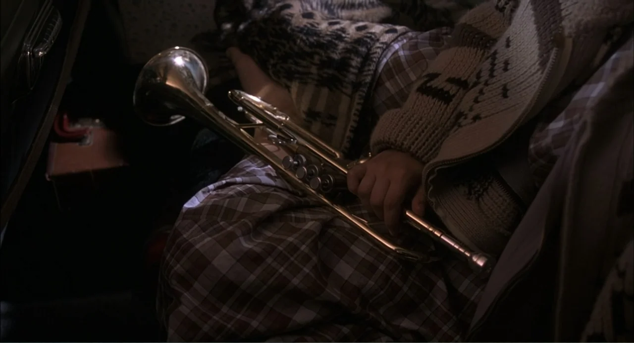 Wild Orchid II: Two Shades of Blue (1991) movie still: closeup — A person sits inside a vehicle while holding a brass trumpet on their lap. The…