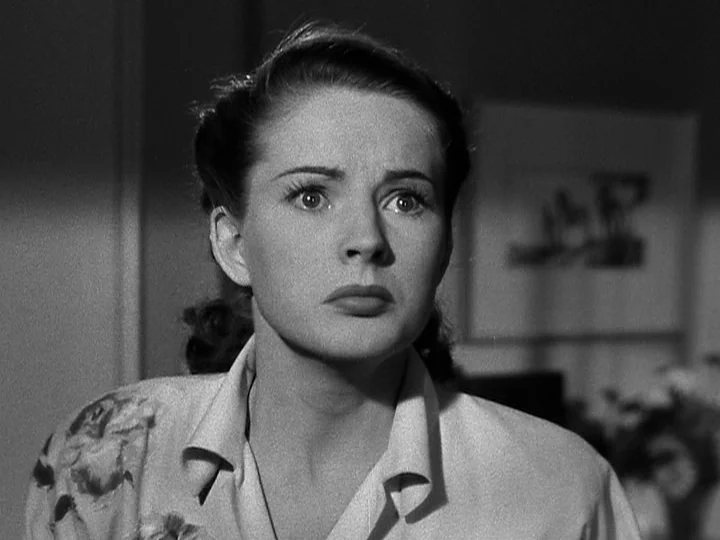 Nightmare Alley (1947) movie still: closeup — A dimly lit indoor space with a framed picture visible in the blurred background. A young woman with…