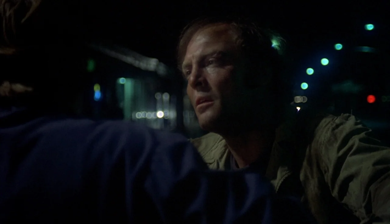 Fat City (1972) movie still: medium — A dark urban environment at night with distant out-of-focus street lights in the background. A man in a tan…