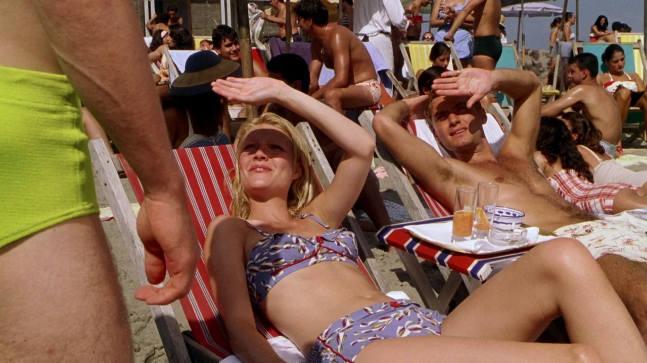 The Talented Mr. Ripley (1999) movie still: medium — A crowded public beach with many people lounging in striped chairs under the sun. A young man…