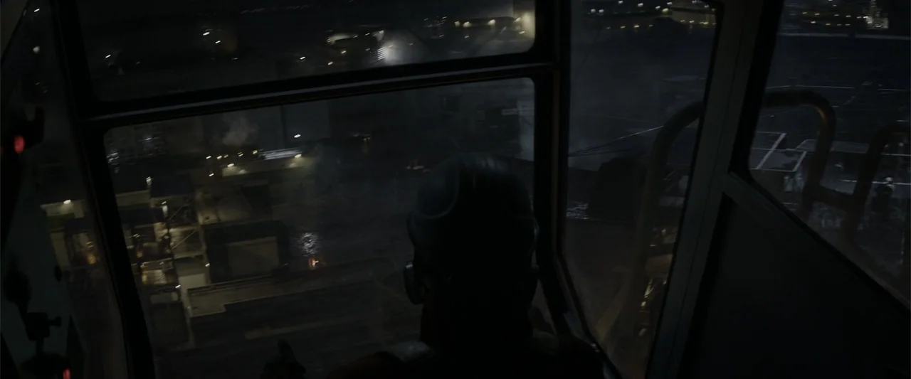 Godzilla (2014) movie still: medium — An interior view from inside a crane cabin overlooking a dark industrial construction site. A lone worker in a…
