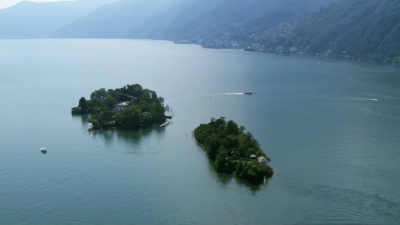 The Alps from Above: Symphony of Summits (2014) movie still: establishing — An aerial view shows two forested islands situated within a large…