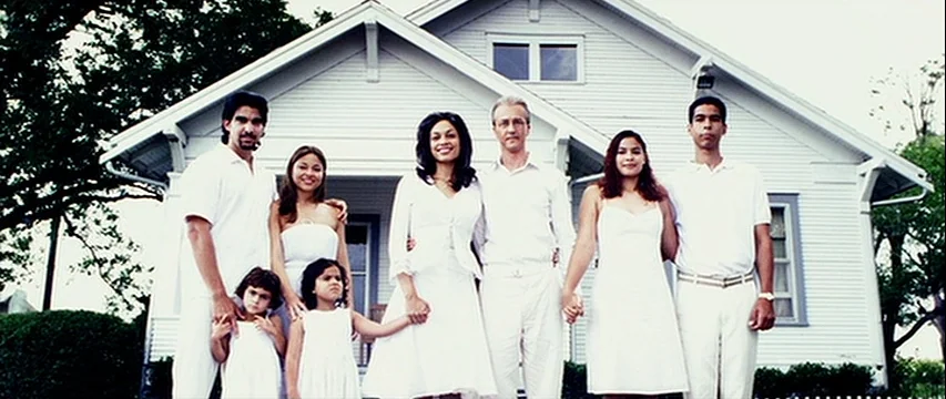 25th Hour (2002) movie still: fullbody — A multi-generational family stands in front of a white wood-paneled residential building. They are…