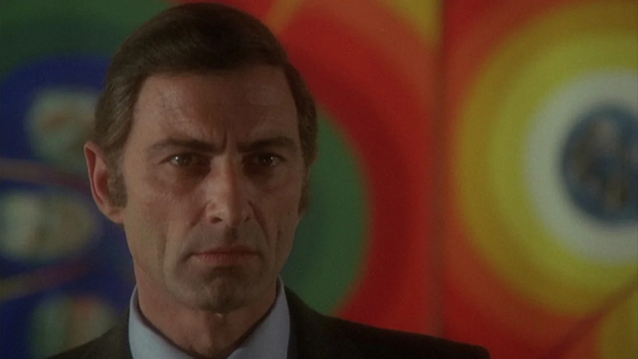 The Black Belly of the Tarantula (1971) movie still: closeup — An interior wall features large colorful painted targets of concentric orange and…