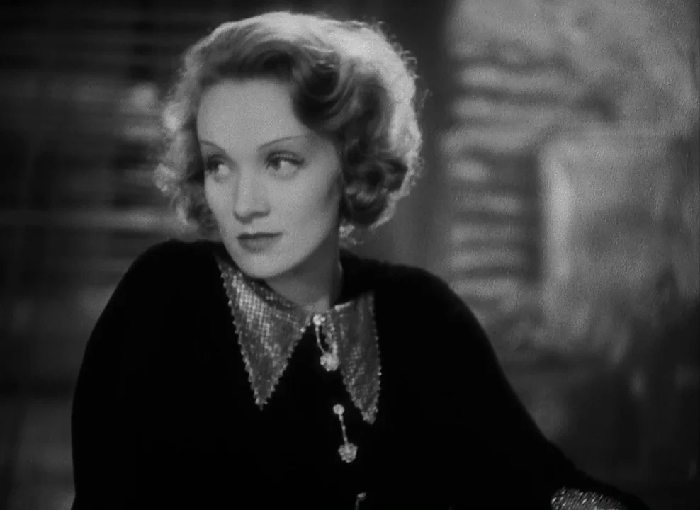 Shanghai Express (1932) movie still: closeup — A dimly lit indoor space with a blurred background suggesting architectural lines or blinds. A blonde…