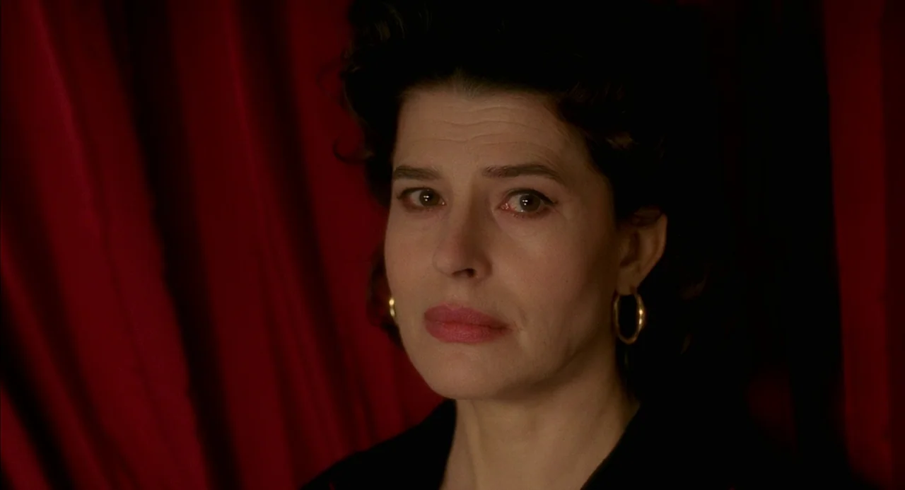 8 Women (2002) movie still: closeup — A woman stands in front of dark, textured red curtains in a theater space. She looks directly into the camera…