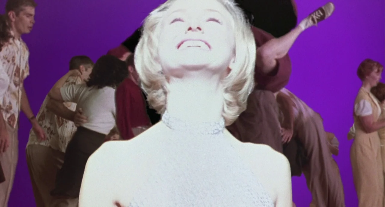 Mulholland Drive (2001) movie still: medium — A studio space with a flat purple backdrop stands behind multiple pairs of dancers. A woman in a…