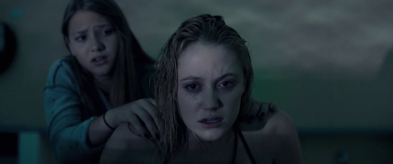 It Follows (2015) movie still: medium — A dimly lit indoor swimming pool environment features water-slicked surfaces and dark murky backgrounds. One…