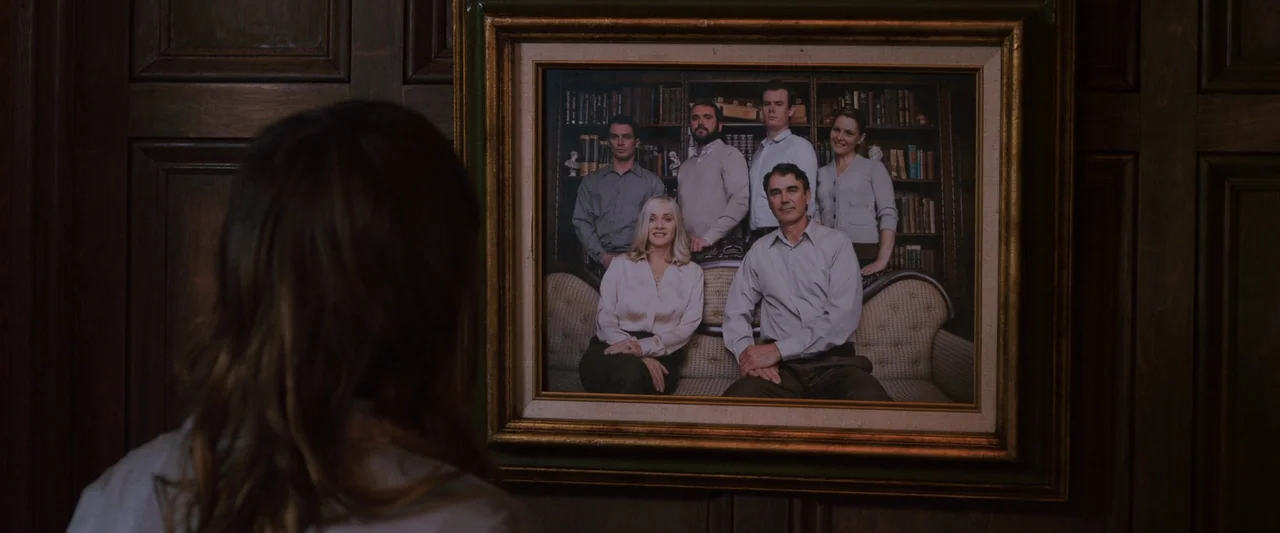 You’re Next (2013) movie still: medium — A dark, wood-paneled wall holds a large, ornate framed photograph of a family group. The foreground…