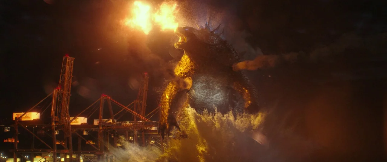 Godzilla Vs. Kong (2021) movie still: wide — A massive kaiju emerges from dark ocean water next to a commercial shipping terminal. The creature…