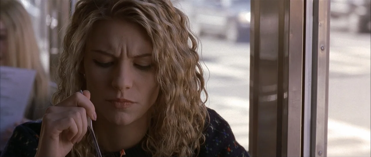 Igby Goes Down (2002) movie still: closeup — A diner interior with a window view of a blurred street. A young woman with curly hair looks down while…
