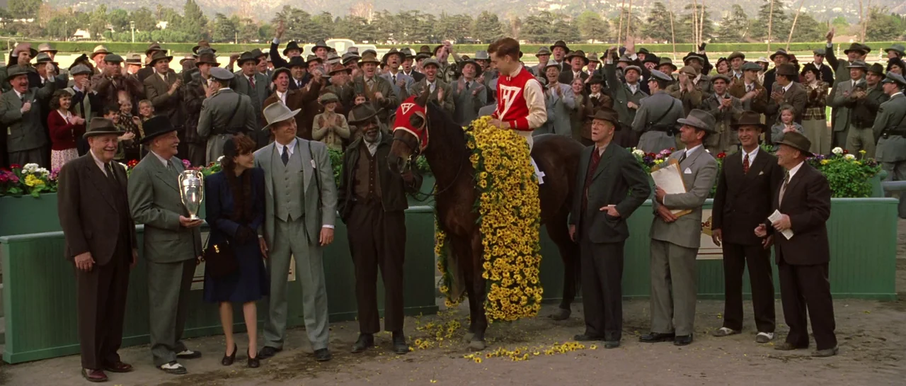 Seabiscuit (2003) movie still: fullbody — A sunny racetrack winner's circle features a crowd of men in vintage 1940s suits. A jockey sits on a…