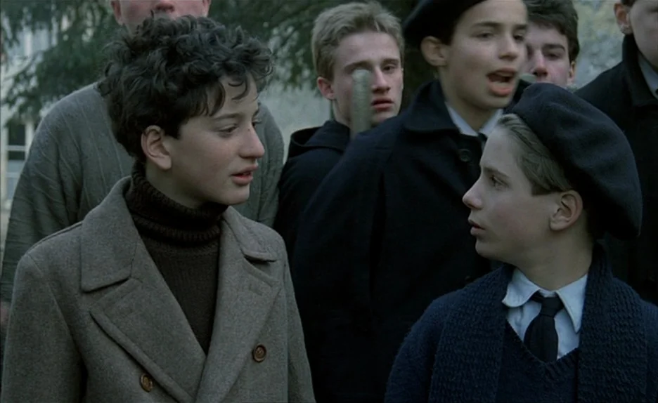 Au Revoir Les Enfants (1987) movie still: medium — A group of teenage boys in 1940s style clothing stands outdoors. Two boys in the foreground look…