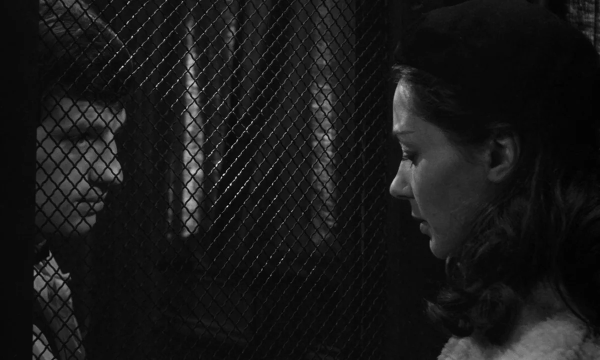 Léon Morin, Priest (1961) movie still: medium — A dark, enclosed space separated by a thick metal diamond-patterned wire mesh screen. A man and a…
