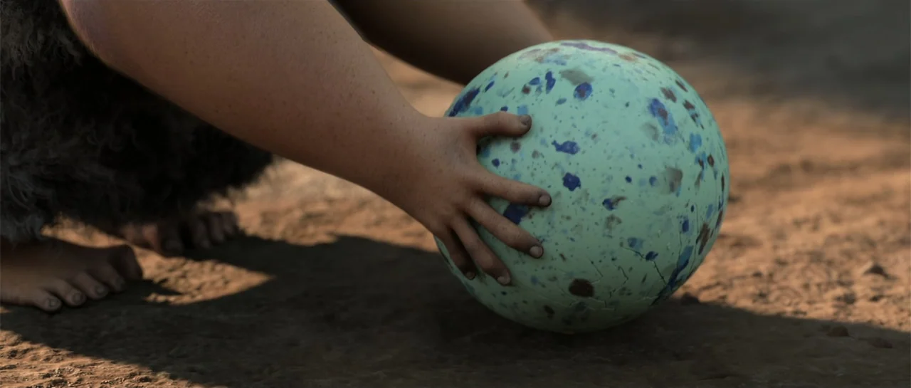The Croods (2013) movie still: closeup — A dusty patch of earth serves as the backdrop for a large mottled orb. A child reaches forward with a…