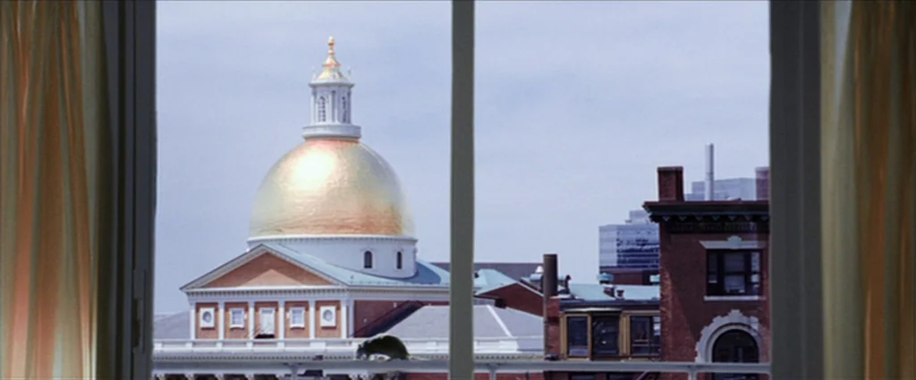 The Departed (2006) movie still: wide — A view through a window showing the Massachusetts State House dome in Boston. The golden dome rises above…