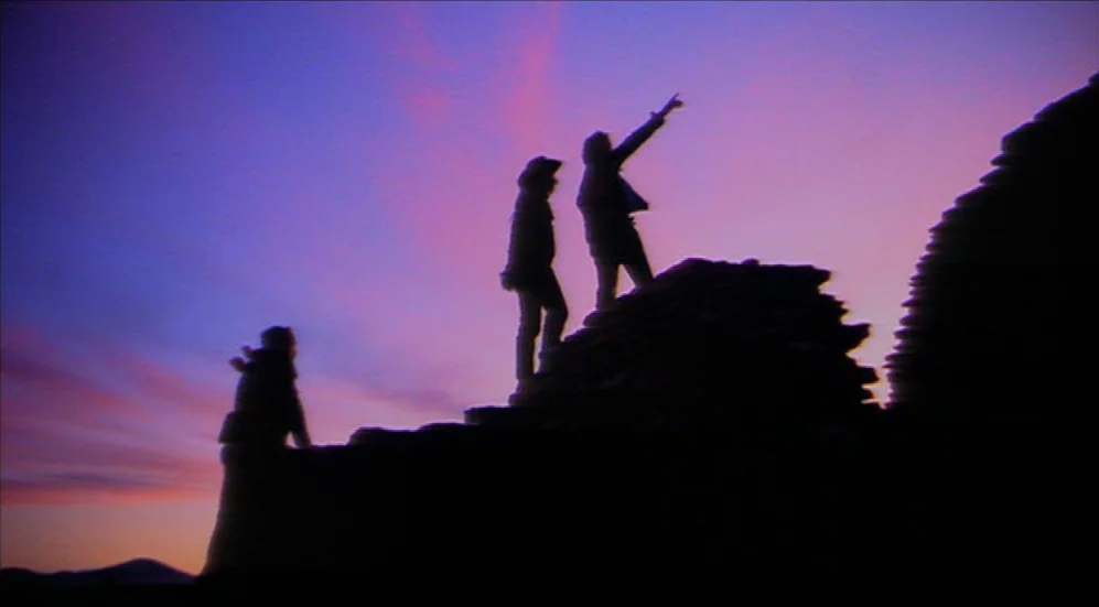 Easy Rider (1969) movie still: wide — A rocky outcrop stands against a vibrant twilight sky filled with purple and orange hues. Three individuals…