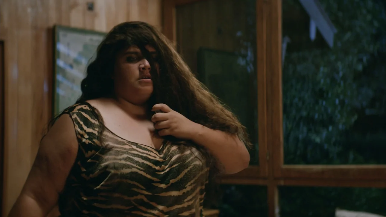 That's Not Cheating (2016) movie still: medium — A dimly lit room with wood-paneled walls features a large window in the background. A woman with…