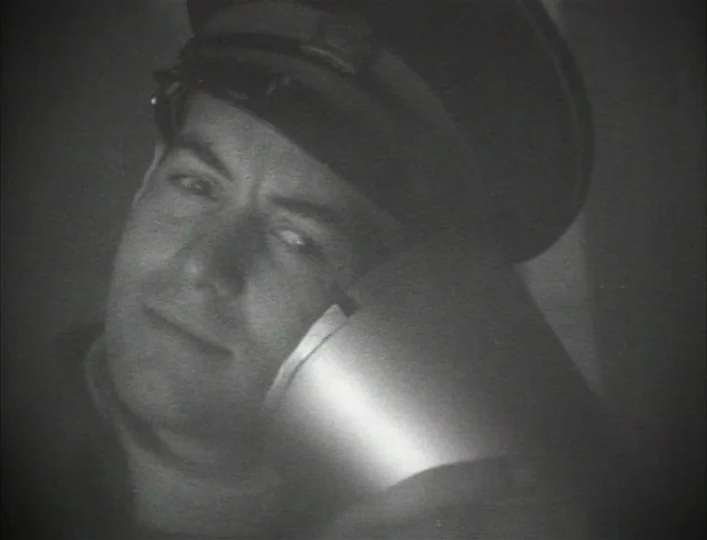 Archangel (1990) movie still: closeup — A man in a military cap holds a large metallic telephone receiver. He is pressed close to the device while…