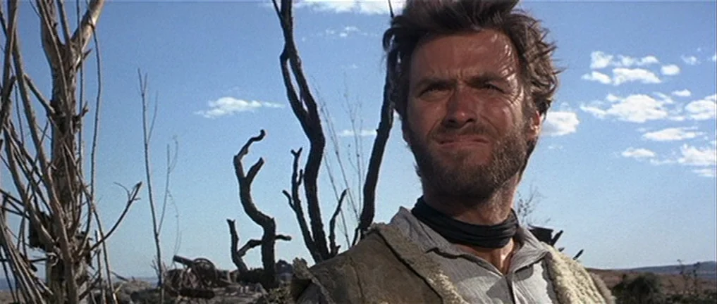 The Good, The Bad And The Ugly (1966) movie still: medium — A dry desert landscape with skeletal, leafless trees stands under a bright blue sky. A…