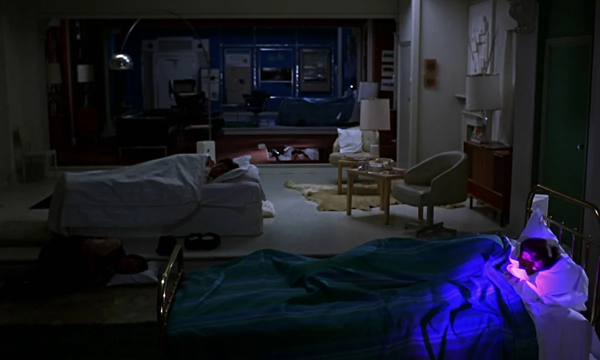 Help! (1965) movie still: wide — A mid-century modern bedroom features multiple beds and minimalist furniture in low light. Two figures lie in…