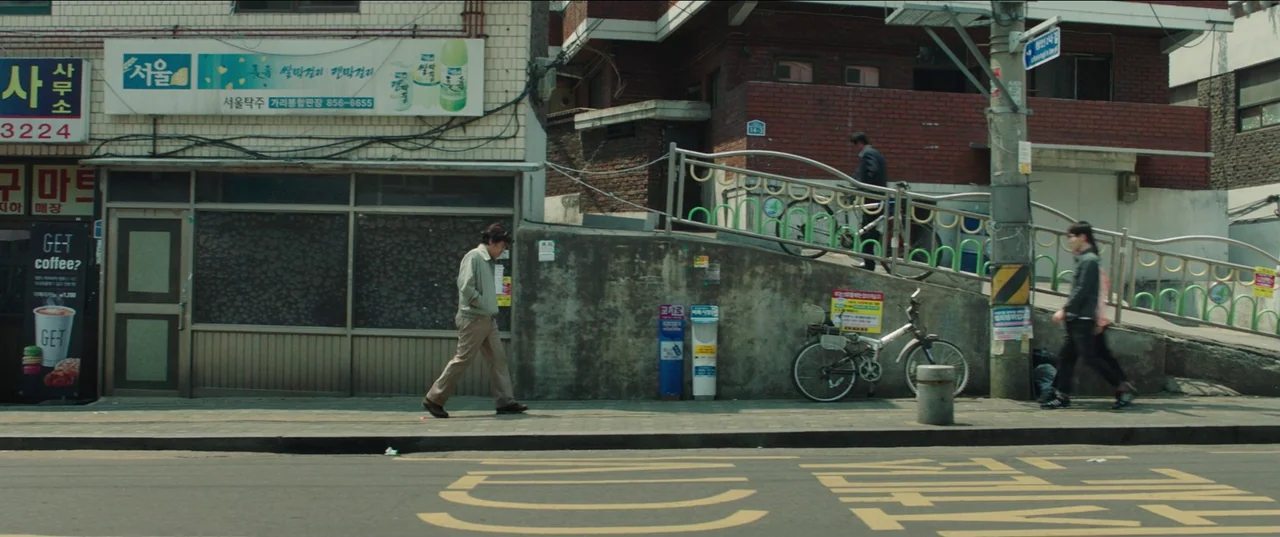 Psychokinesis (2018) movie still: wide — A quiet urban street in South Korea features a concrete ramp and brick buildings. Three men move…