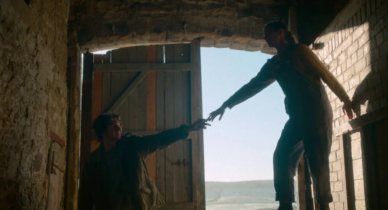 Dark River (2017) movie still: fullbody — A rustic stone-walled barn has a wide-open wooden door looking out toward distant hills. A man and a woman…
