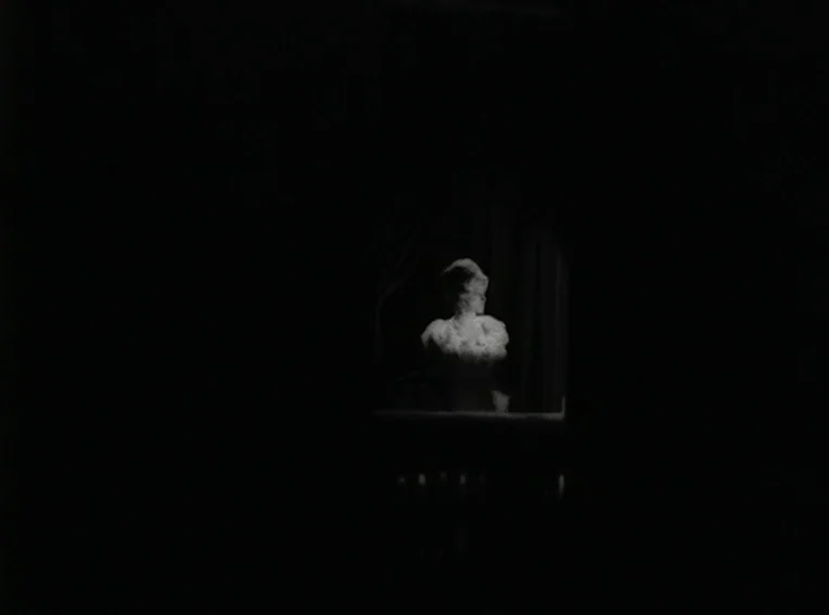 Cuadecuc, Vampir (1971) movie still: wide — A dark, empty space frames a brightly lit balcony area with dark curtains. A woman in a light dress…