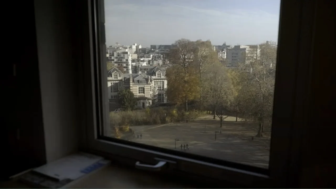 Brexit: Behind Closed Doors (2019) movie still: establishing — An urban landscape view from inside a room looking out of a window. Trees and a small…